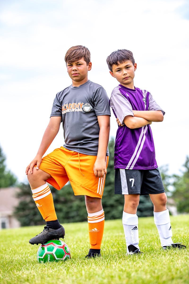two boys on a soccer field one with a foot on a ball
